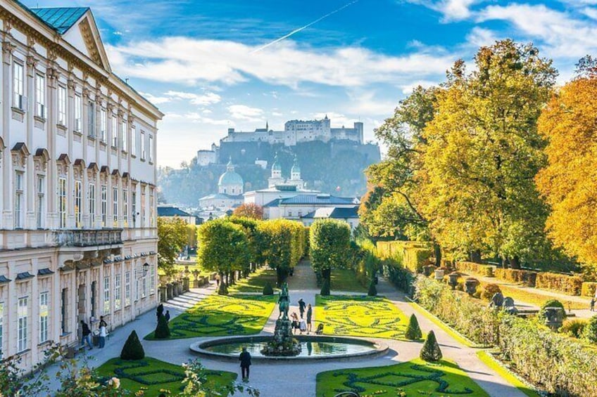 Ein gepflegter formaler Garten mit Rasenflächen, einer Fontäne und einem historischen Gebäude im Hintergrund. 4