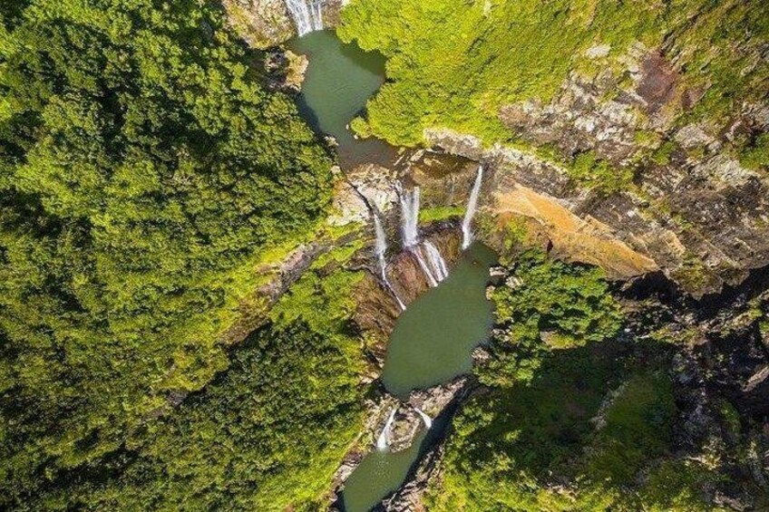 Ein Wasserfall stürzt in einen Fluss, umgeben von dichtem Grünland. 1