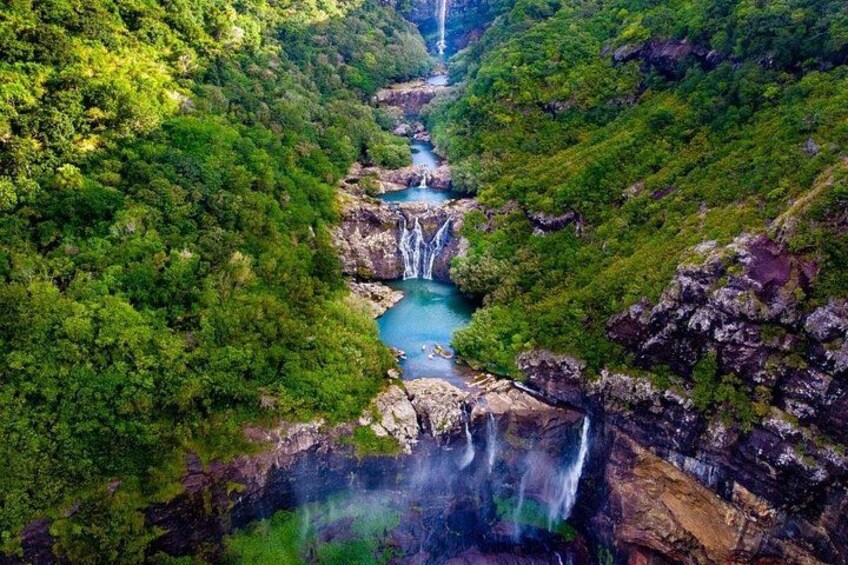 Ein Wasserfall stürzt in einen Fluss, umgeben von üppigem Grün. 3