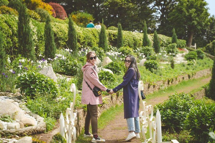Dos personas tomadas de la mano en un sendero de jardín rodeado de follaje y flores. 4