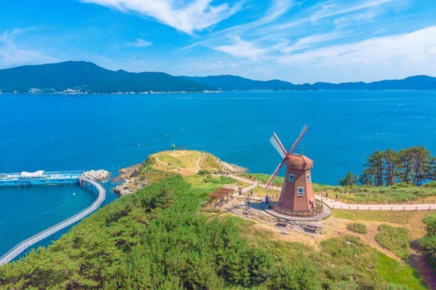 Un molino de viento en una colina con vistas a un cuerpo de agua, un puente y montañas distantes. 1