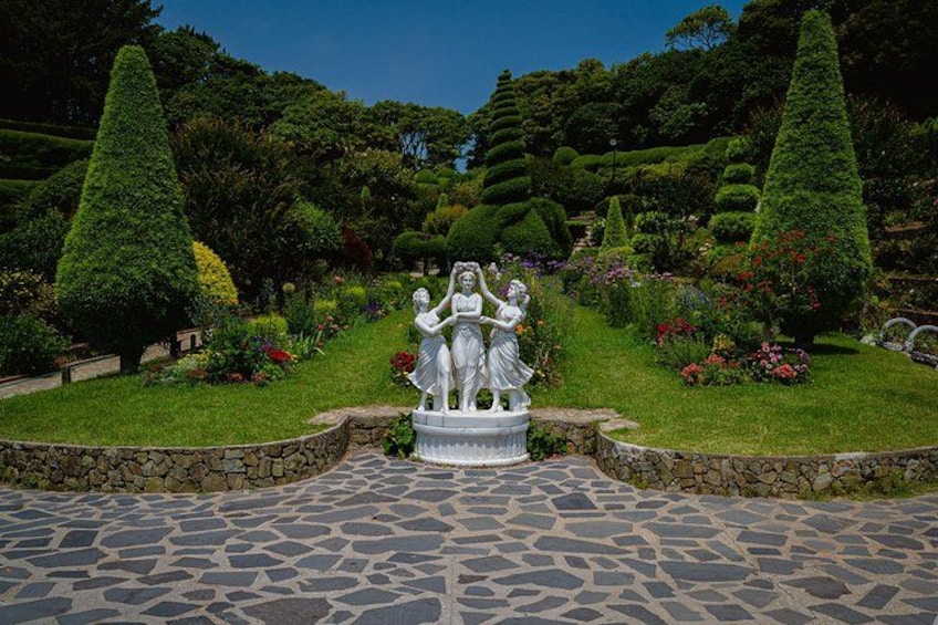 Un jardín con una estatua central, setos bien recortados y un camino de piedra. 5