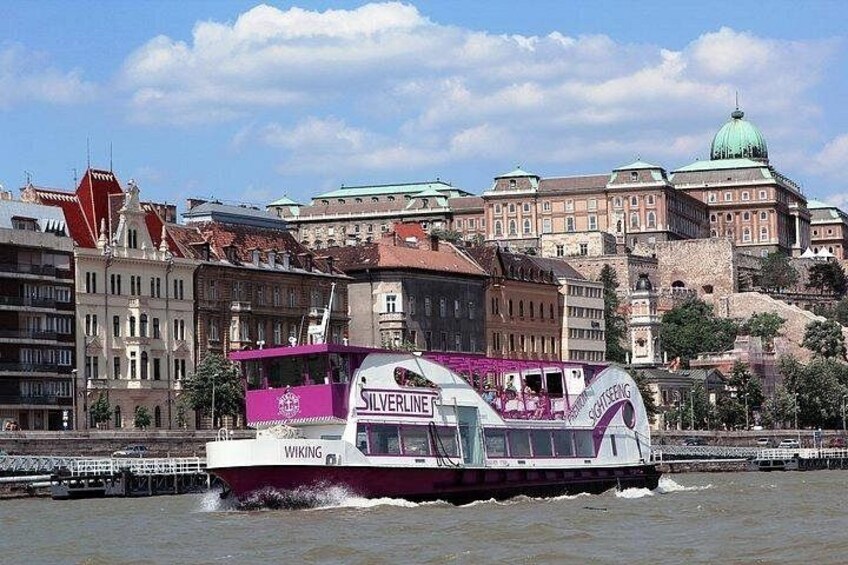 A boat named 'Silverline' with 'Wiking' written on the side, moving on a river with historic buildings in the background. 2