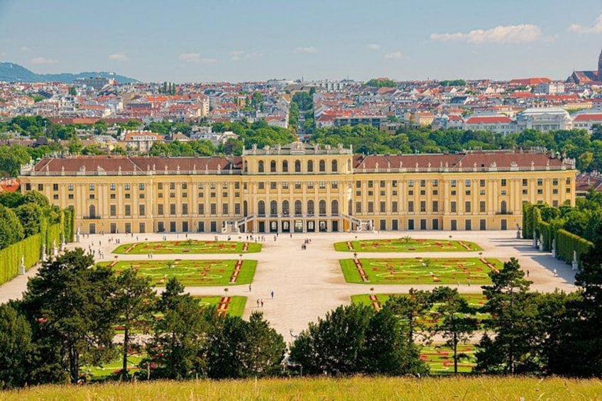 A large historic building with symmetrical gardens and a cityscape in the background. 2