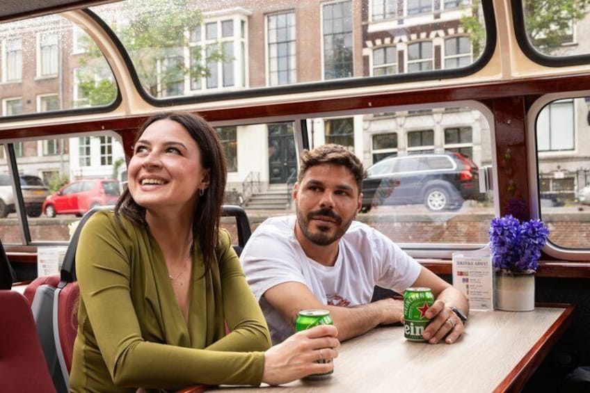 Two people sitting at a table inside a vehicle with a view of buildings and parked cars outside. 2