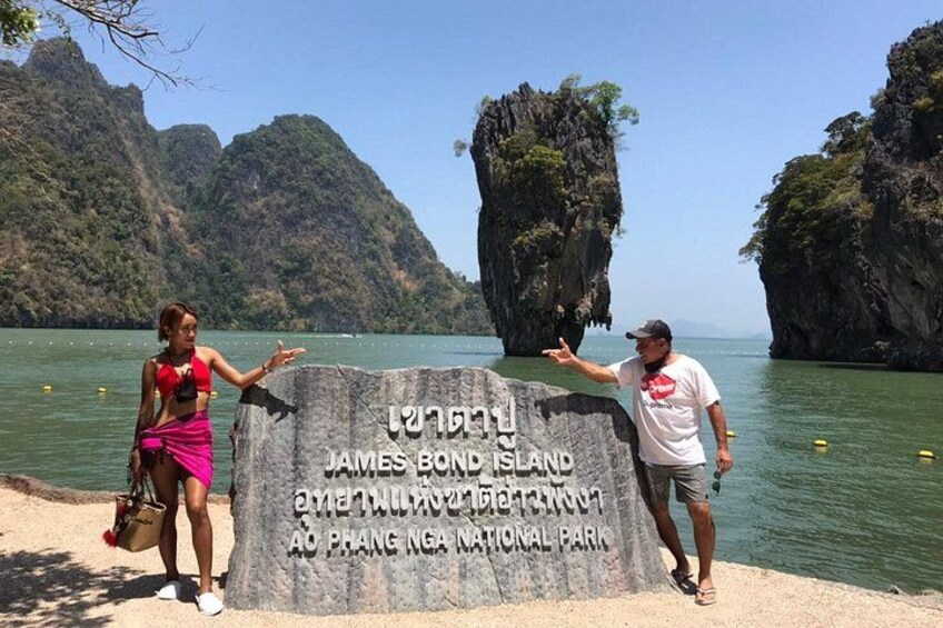 A sign with text, two people, and a body of water with rock formations. 4