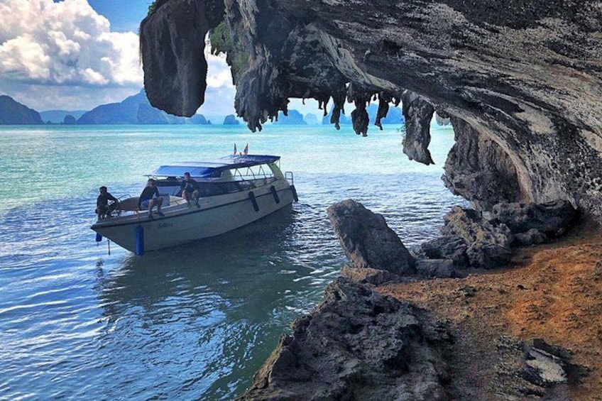 A boat near a rocky cave entrance with clear water and distant mountains. 3