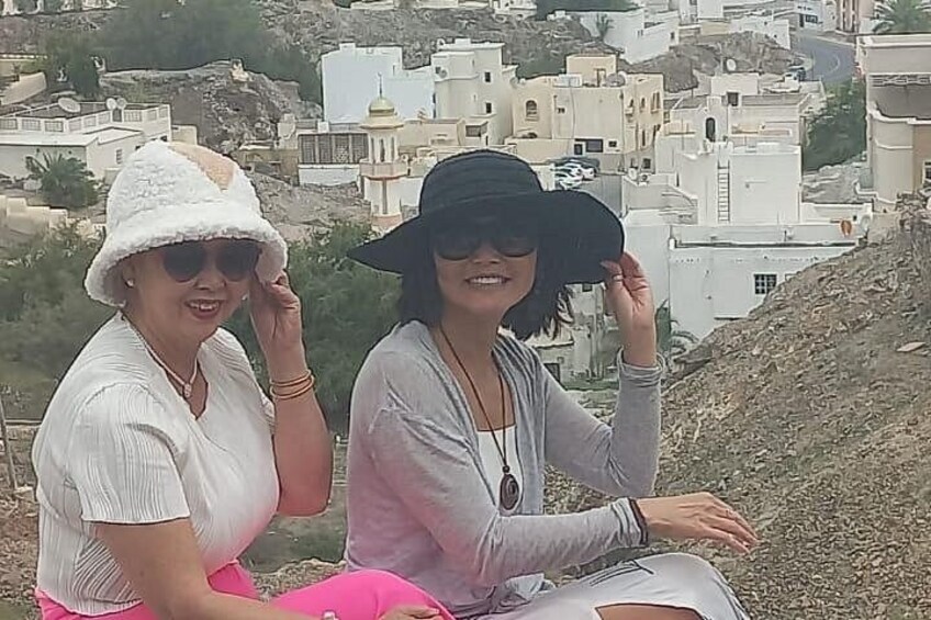 Two people sitting on a hill with a view of white buildings in the background. 2