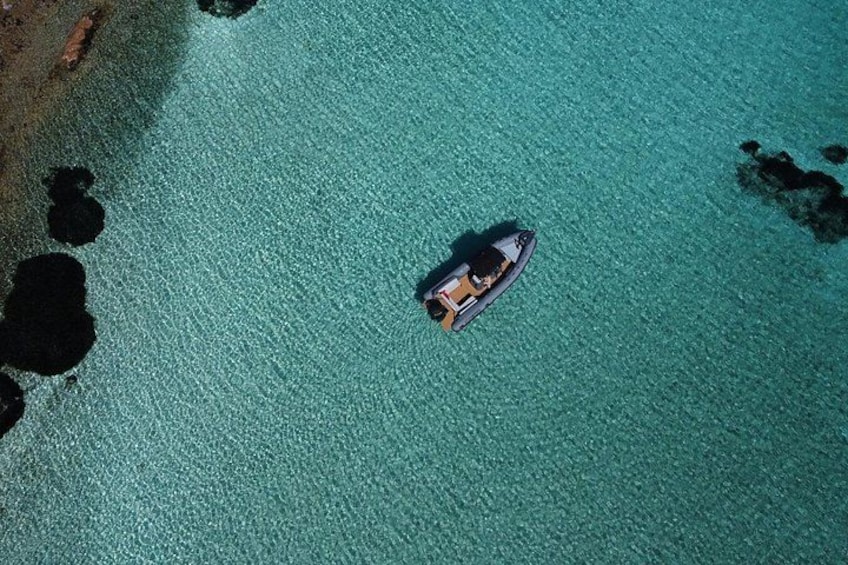 A small boat on turquoise water with a rocky shoreline. 2
