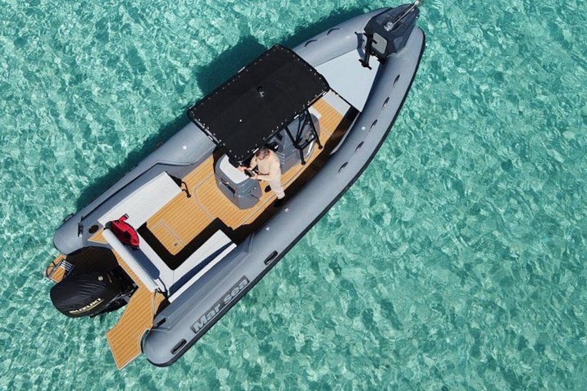 A small inflatable boat with a person seated at the helm, floating on clear turquoise water. 1