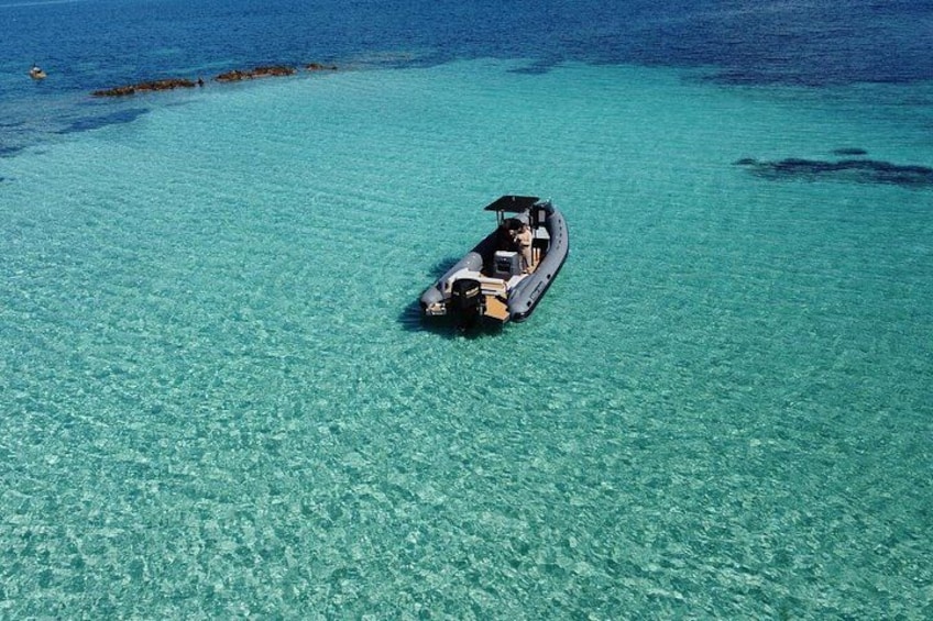 A boat on clear turquoise water with a rocky outcrop in the distance. 3
