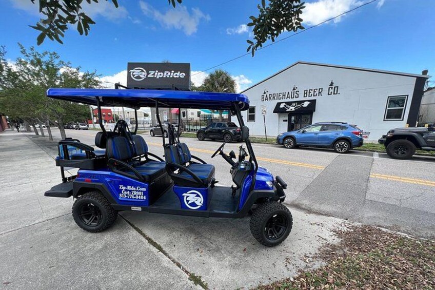 A blue golf cart parked on a sidewalk with a building labeled 'Barricaus Beer Co.' in the background. 1