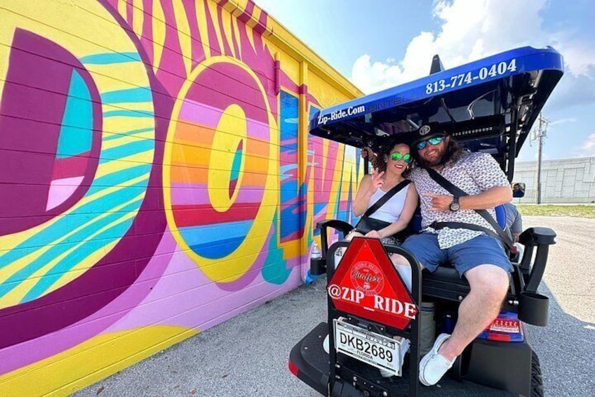 A colorful mural with large circular patterns and a golf cart with a license plate and a company logo. 3