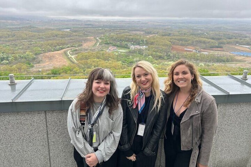 Three people standing on a rooftop with a view of a valley. 3