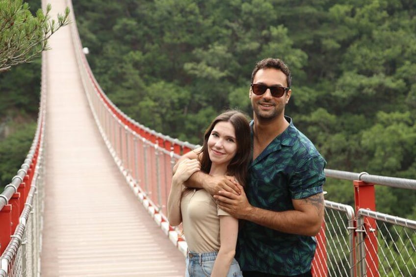 A couple standing on a bridge with a forested landscape in the background. 1