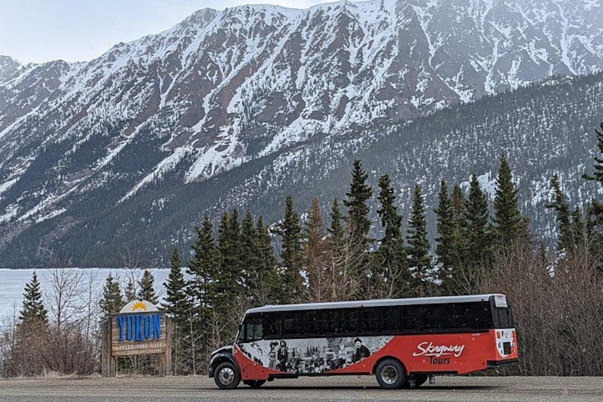 Un autobus rouge et noir, sur lequel on pouvait lire « Skaguay Tours », était garé devant une chaîne de montagnes dont les sommets étaient couverts de neige, avec un lac en contrebas. 5