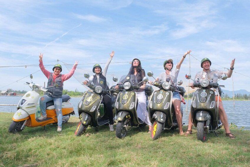 Cinq personnes sur des scooters au bord d’un lac, avec des arbres en arrière-plan. 1