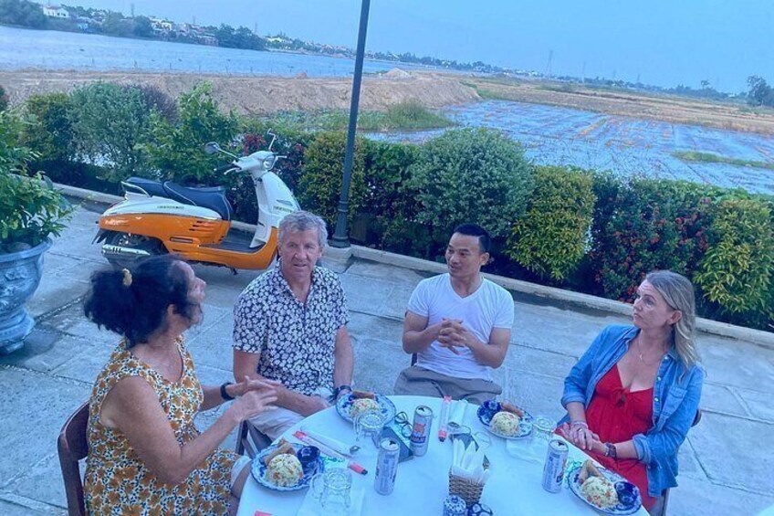 Un gruppo di persone cena a un tavolo all'aperto con vista panoramica sulla spiaggia e sull'oceano. 3