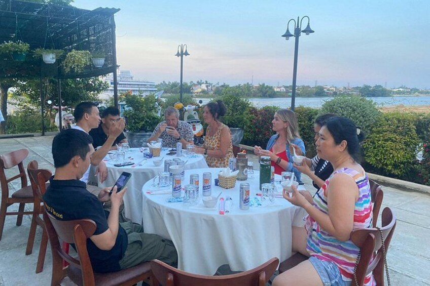 Un groupe de personnes est assis à une table en plein air, devant un restaurant, et profite de la vue sur la mer. 3