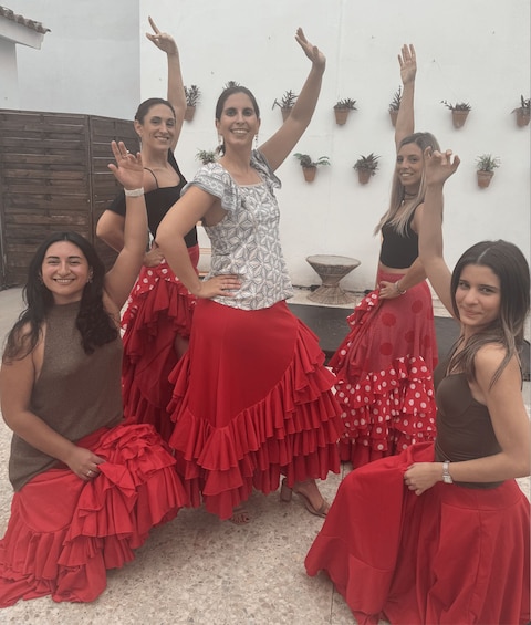 A group of women in red dresses with ruffles, standing and sitting in an outdoor setting with a white wall and potted plants in the background. 2