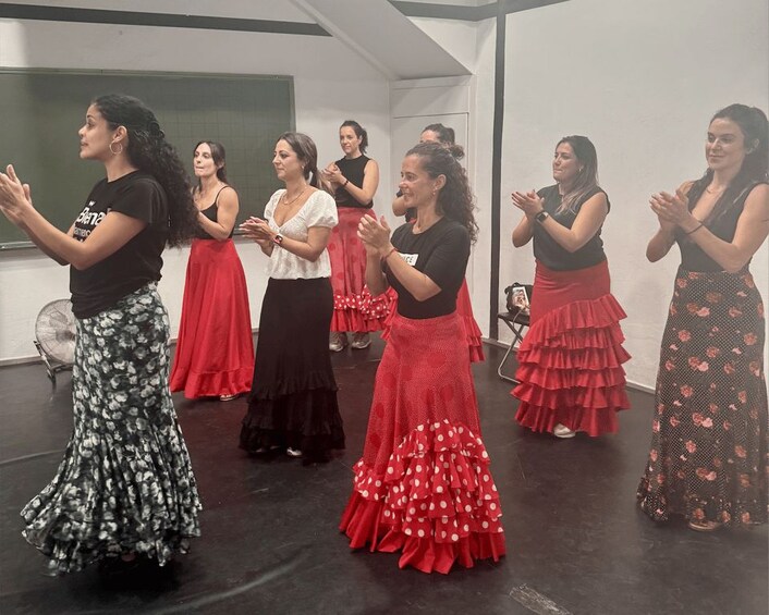 A group of women in dance practice, wearing traditional skirts, in a studio with a black floor and white walls. 3