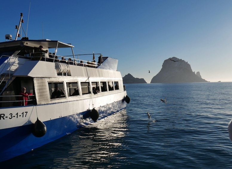 A boat with passengers, calm sea, and distant rocky cliffs. 1