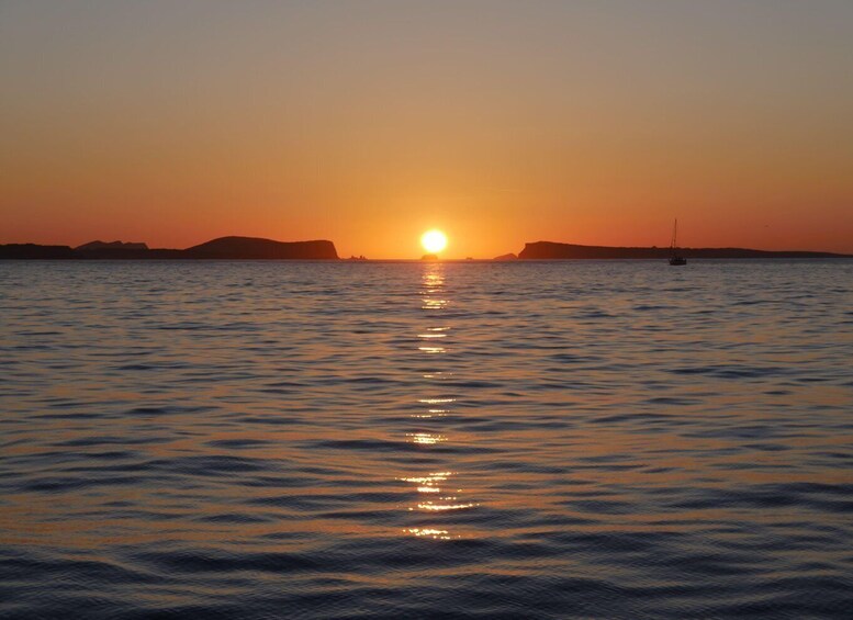 A sunset over calm water with a silhouette of land in the distance and a boat on the horizon. 4