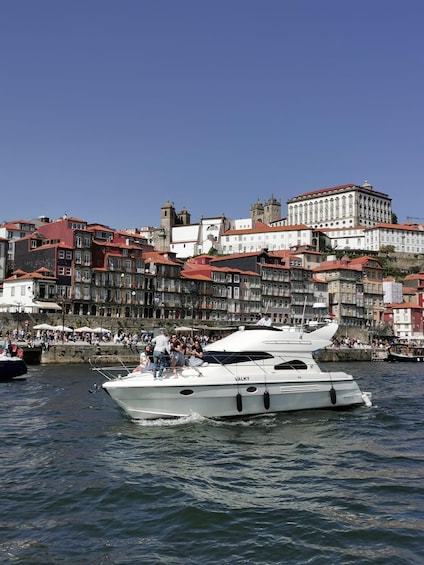 Eine weiße Yacht namens VALKY auf dem Wasser mit Personen an Deck, einer Menschenmenge am Steg und historischen Gebäuden im Hintergrund. 1