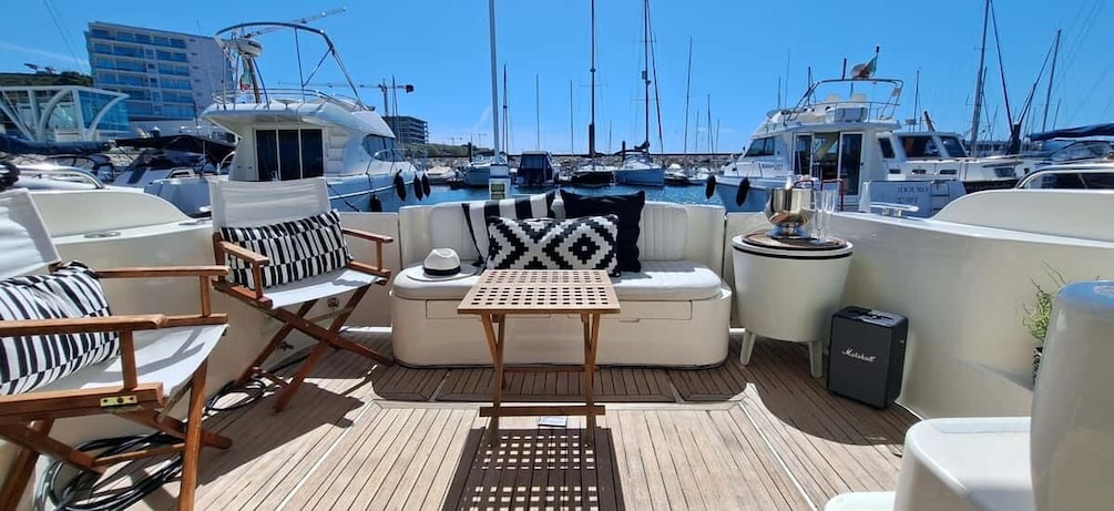 Ein Yachthafen mit vertäuten Booten, eine Lounge mit einer Couch und Sesseln sowie ein Lautsprecher auf dem Deck. 1