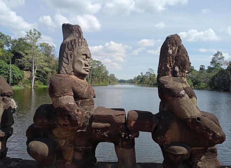 Une structure en pierre ornée d’un visage sculpté, entourée d’eau et d’arbres. 3