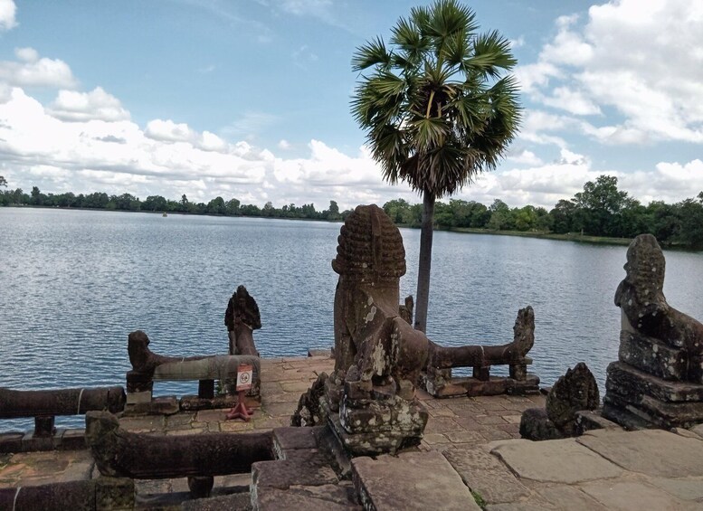 Une structure en pierre, avec un palmier au premier plan, une étendue d’eau et un ciel nuageux. 2