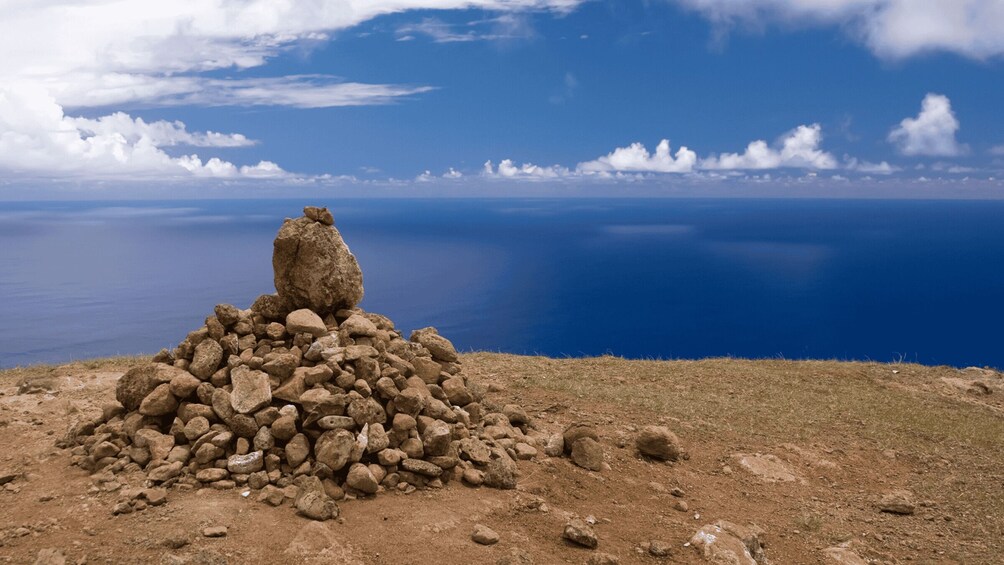A rocky hill with a cairn on top, overlooking a vast body of water under a clear sky. 2