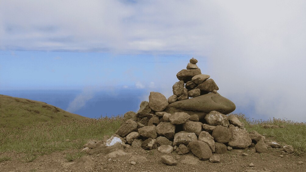 A cairn on a grassy hill with a clear sky and ocean in the background. 3