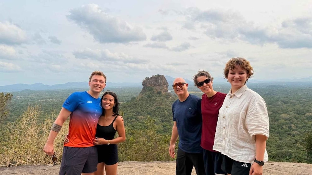 A group of people standing on a rocky outcrop with a mountainous landscape in the background. 1