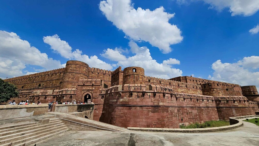 A large, historic fort with red stone walls and a clear blue sky with clouds. 5