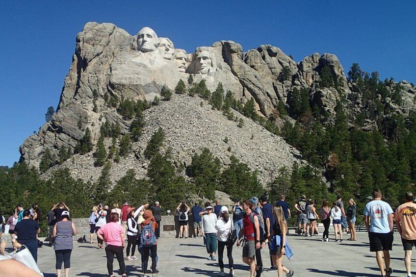 A large crowd of people at a monument with three large statues. 1