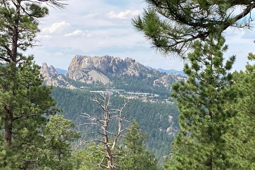A mountain landscape with a prominent rocky peak, surrounded by dense pine trees. 2