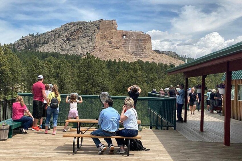 A group of people on a wooden deck overlooking a rocky hill with a fort-like structure. 4