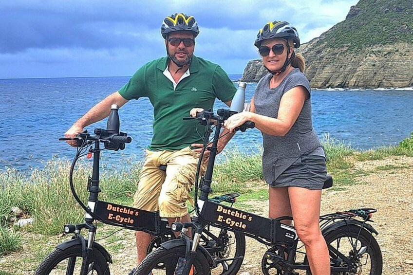 Zwei Personen fahren mit E-Bikes an einer Küstenlandschaft mit Klippen und dem Meer im Hintergrund. 4