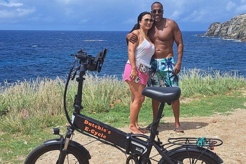 Ein Paar steht an einem Strand neben einem feststehenden E-Bike. 5
