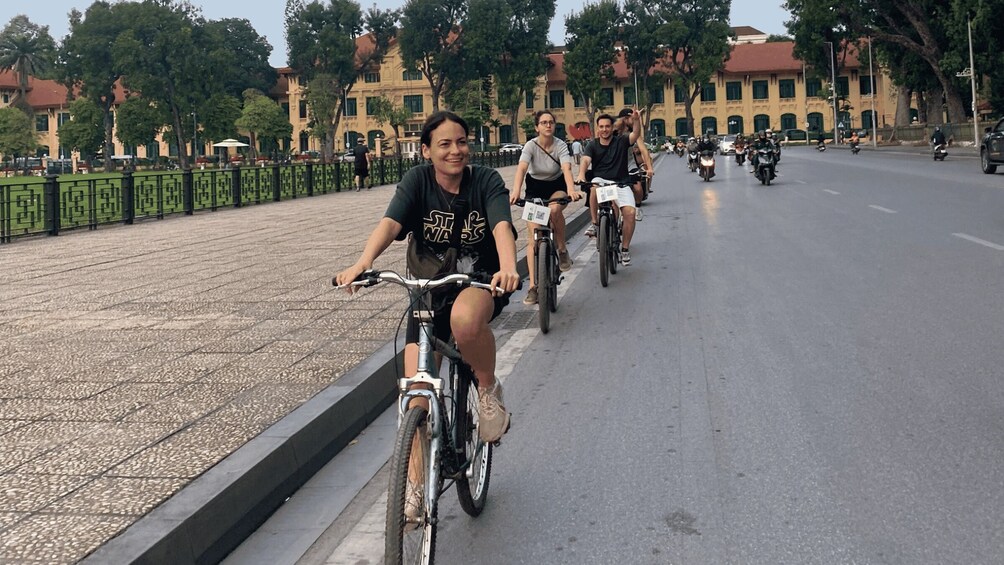 A group of people riding bicycles on a paved path alongside a road with motorbikes in the background. 5