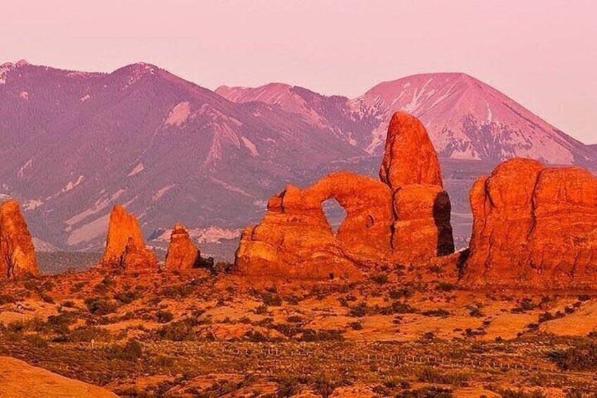 A desert landscape with prominent red rock formations and a mountain range in the background. 1