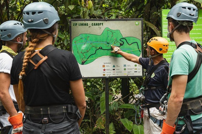 A group of people wearing helmets and harnesses, standing near a map titled 'ZIP Lining - CANOPY' with a green trail marked on it. 3