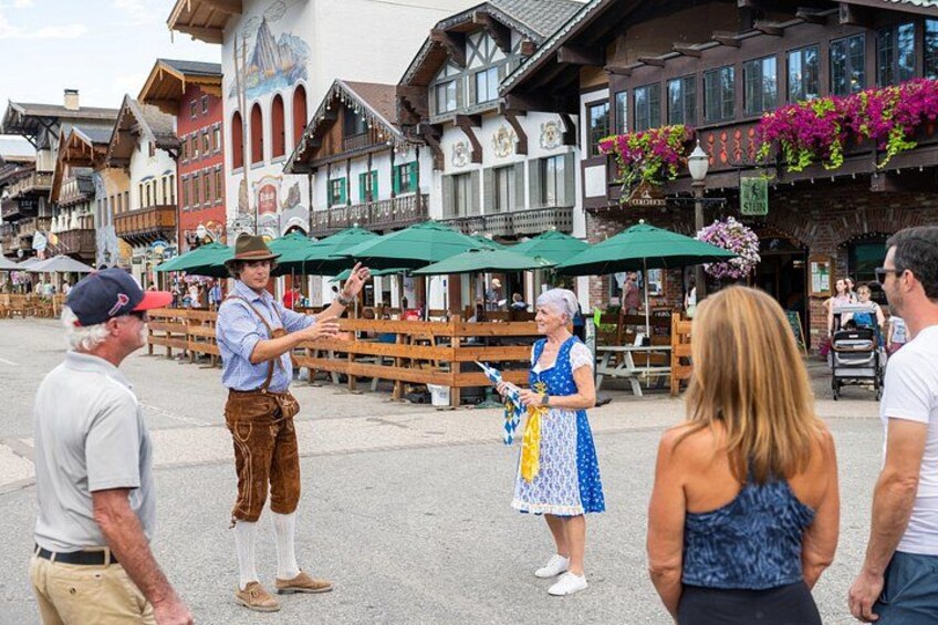 Ein traditionelles bayerisches Straßenszenario mit Holzbauten, Außenplätzen und Menschen in Tracht. 1