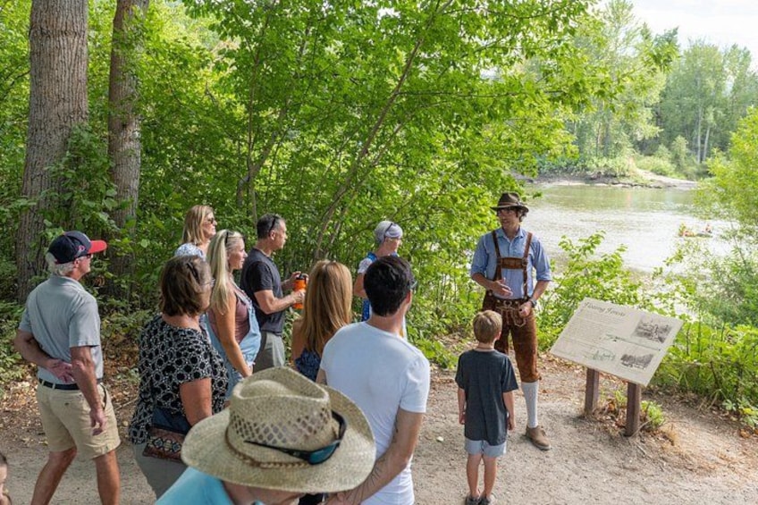 A group of people gathered around a guide near a river, with a signboard in the foreground. 2