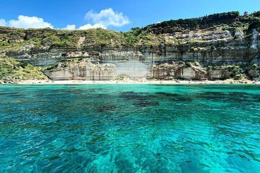 A coastal landscape with clear turquoise waters, rocky cliffs, and a sandy beach. 1