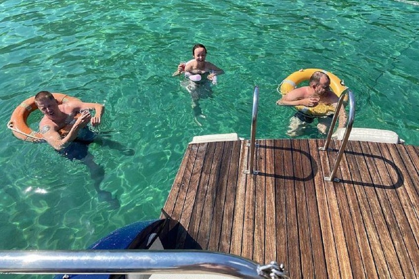 A wooden dock with three people in clear water, wearing life jackets. 3