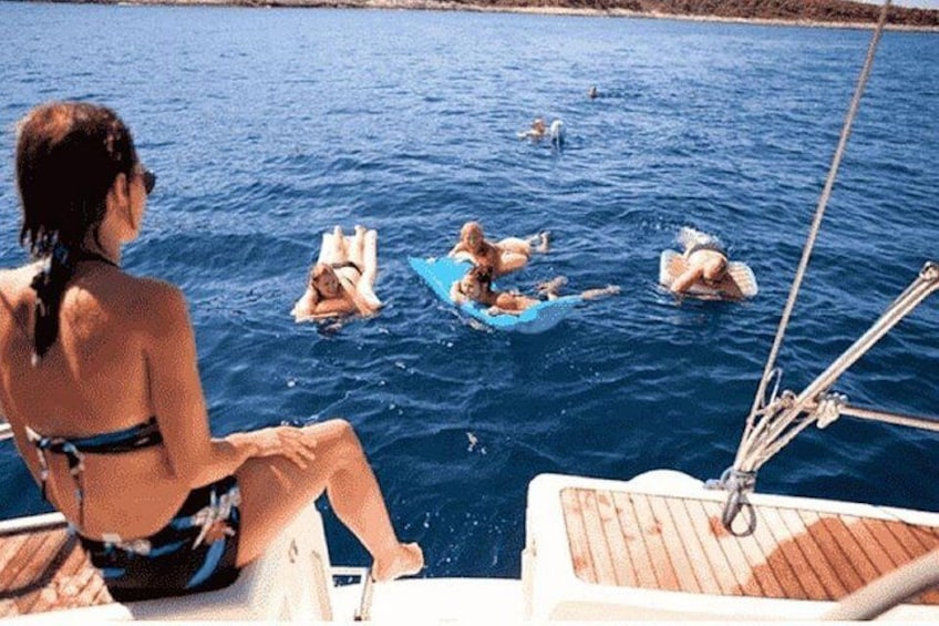 A woman in a bikini sitting on a boat, looking at people swimming in the water. 2