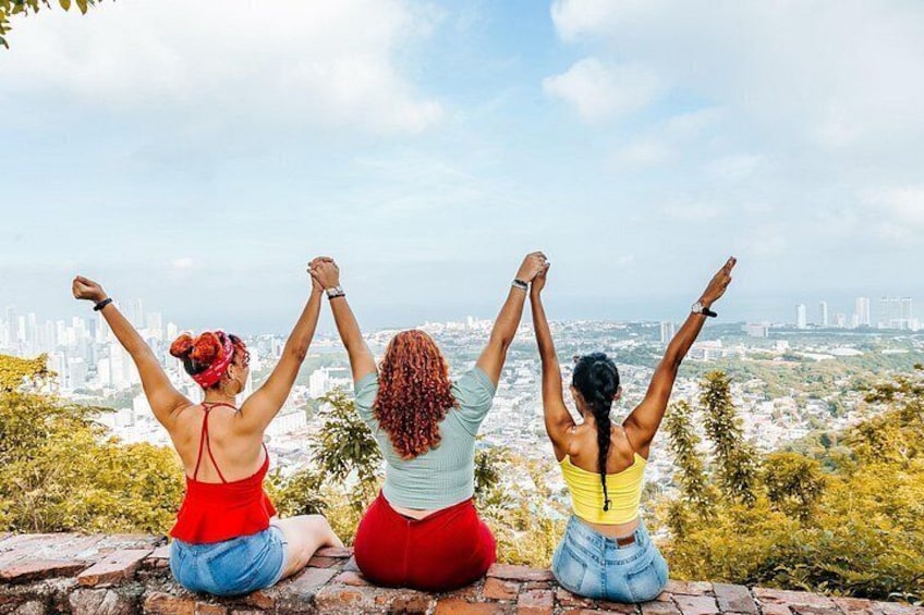 Three people sitting on a brick ledge with their arms raised, overlooking a cityscape. 4
