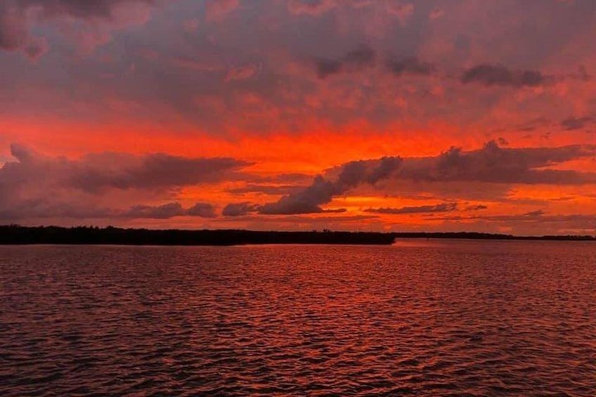 A sunset over a body of water with a silhouette of land in the distance. 1